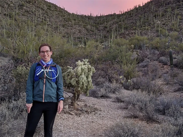 Caitlyn Hall, CUES 2022 Spanning Boundaries Grantee, standing in front of a Sonoran desert landscape at sunset.